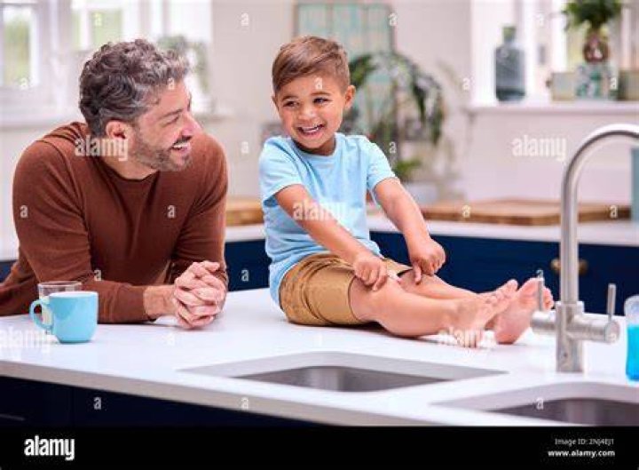 Father sitting on kitchen counter with his little son and having morning coffee. father sitting on kitchen counter with his little son and having morning coffee