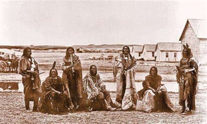 This image shows the Lakota nation people riding horses while holding weapons.